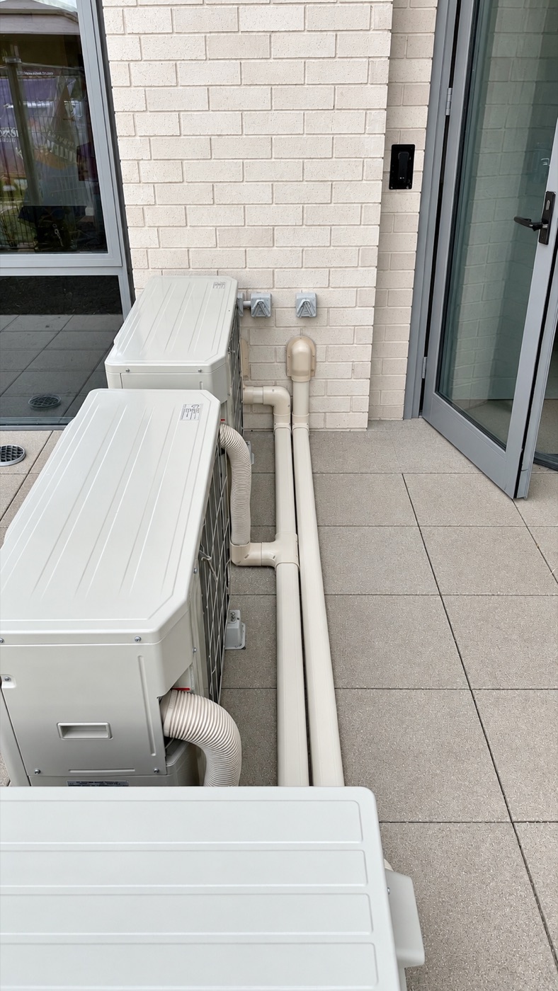 Outdoor heat pump units with insulated pipework run neatly along the wall