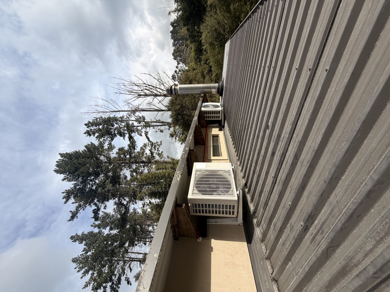 Two outdoor heat pump units installed along the roofline of a bush-surrounded Auckland house